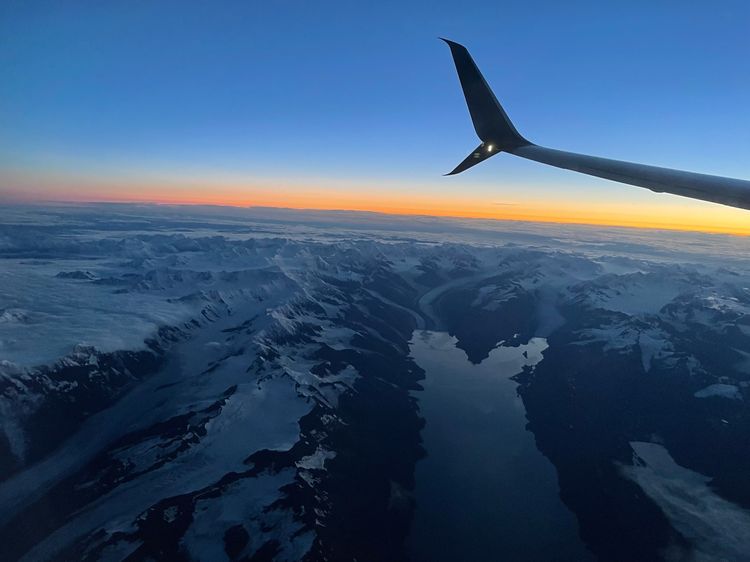 View of glaciers and sunrise with airplane wing in the foreground